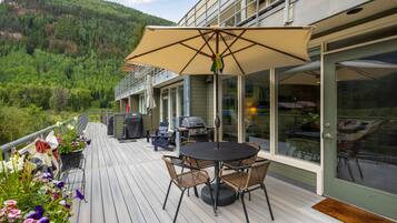 Eine Terrasse mit Gartenmöbeln, einem Grill und Blick auf einen bewaldeten Hang.