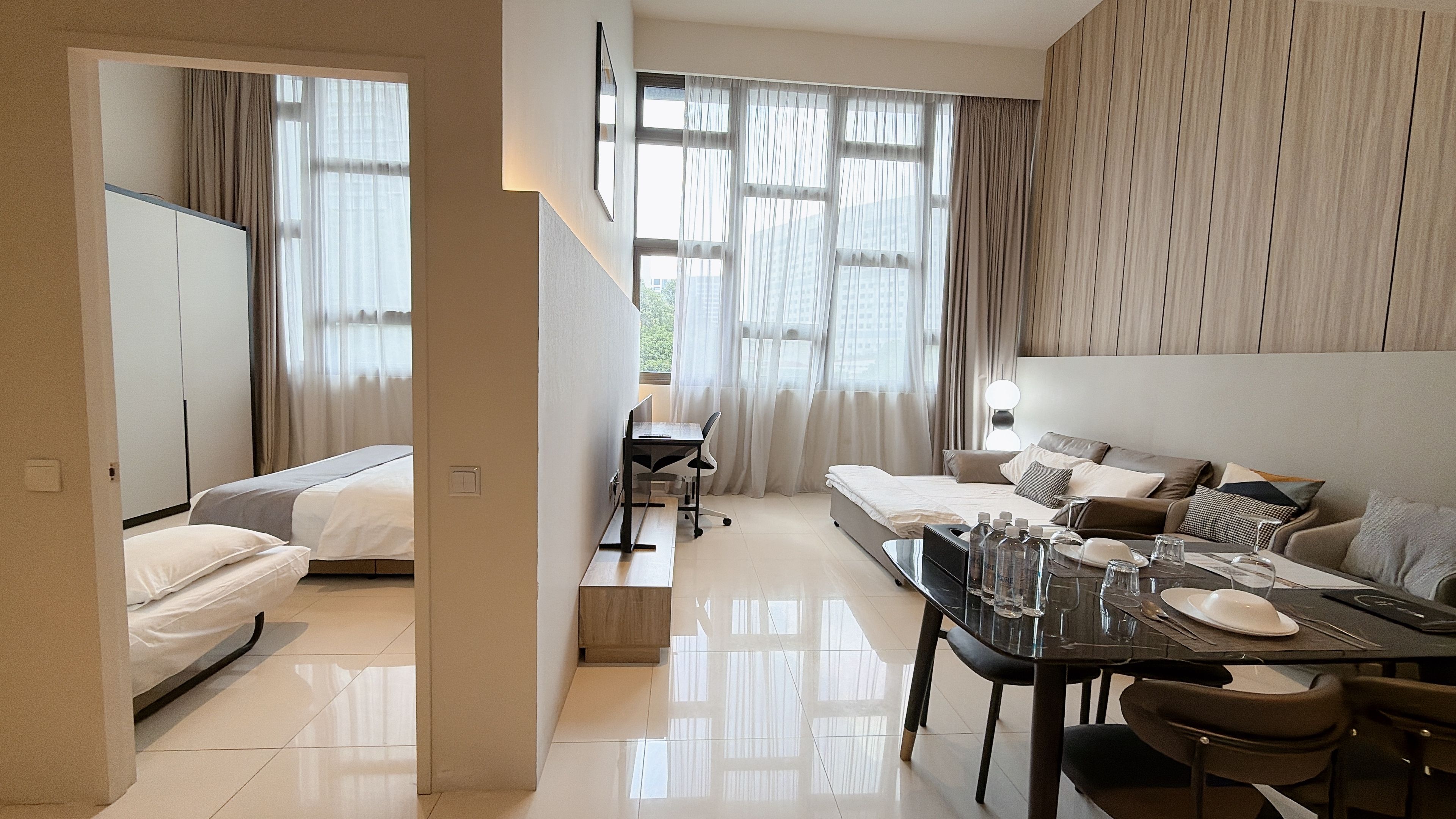 A hotel room with a bed, a desk with a chair, a dining table with chairs, and a sofa.