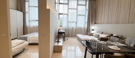 A hotel room with a bed, a desk with a chair, a dining table with chairs, and a sofa.