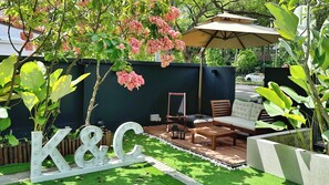A patio with a wooden table and chairs, a large umbrella, and a decorative 'K&C' sign.
