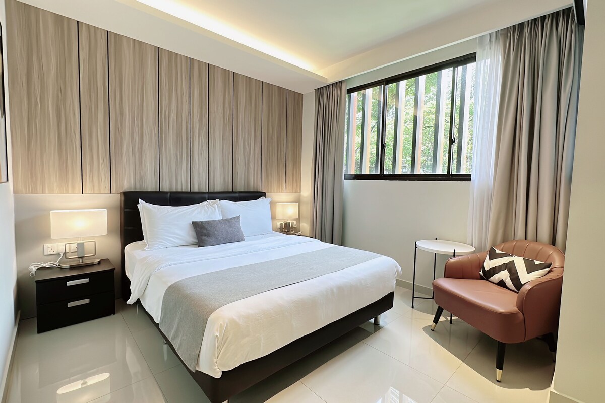 Una habitación de hotel moderna con una cama grande, lámparas de noche, una pequeña mesa redonda y un sillón de cuero.