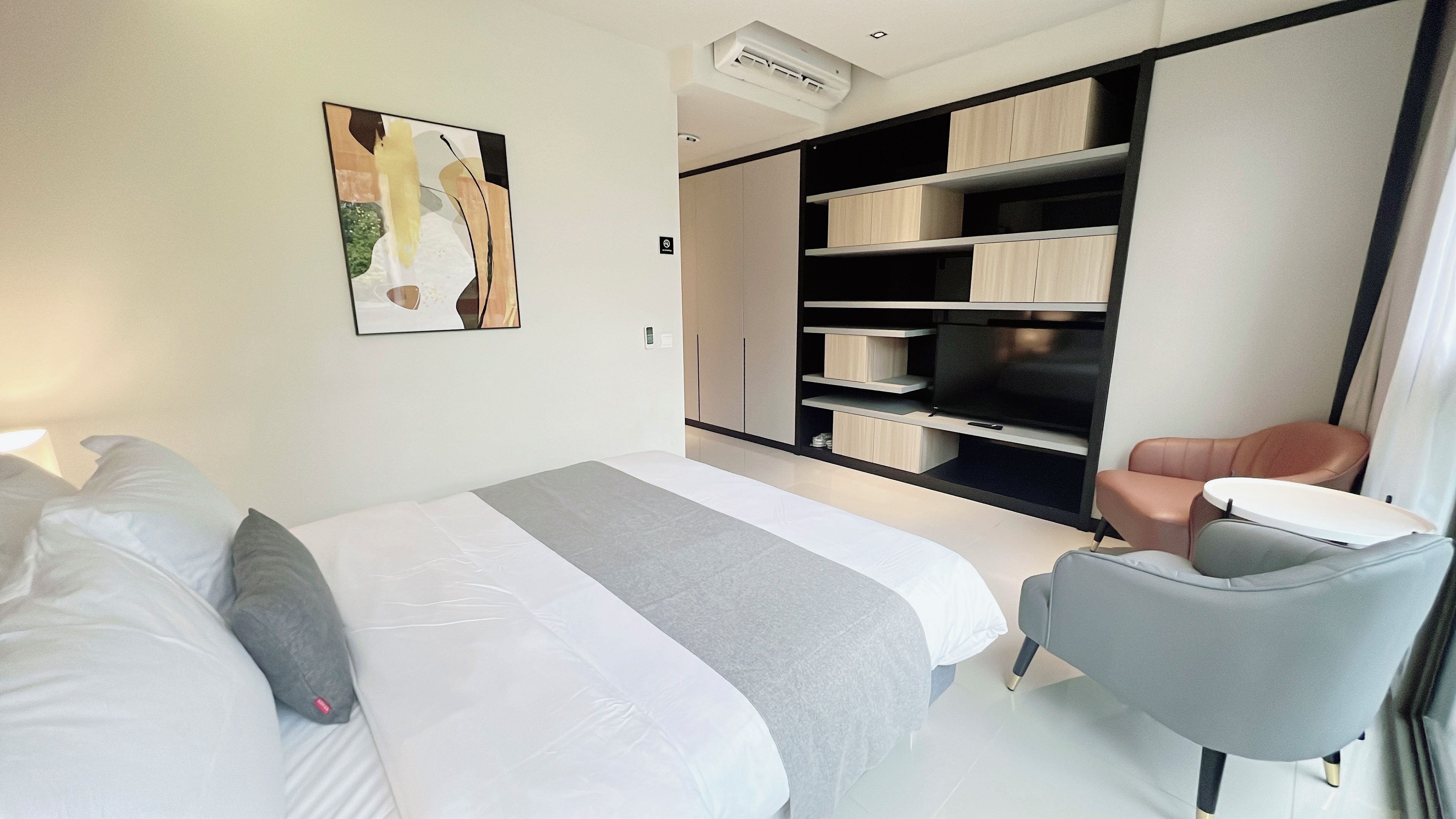 A modern hotel room with a large bed, a seating area with a chair, and built-in storage units.