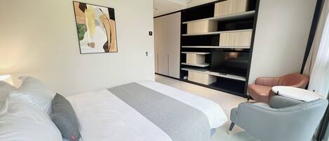 A modern hotel room with a large bed, a seating area with a chair, and built-in storage units.