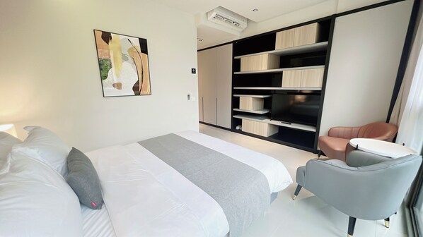 A modern hotel room with a large bed, a seating area with a chair, and built-in storage units.