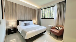 A modern hotel room with a large bed, bedside lamps, a small round table, and a leather armchair. - Moulmein Studios by K&C Serviced Apartment (Singapore)
