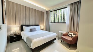 A modern hotel room with a large bed, bedside lamps, a small round table, and a leather armchair. - Moulmein Studios by K&C Serviced Apartment (Singapore)