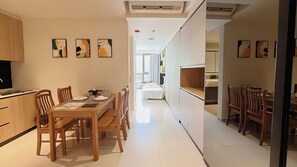 A modern kitchen with wooden cabinets, a dining table set for four, and a corridor leading to a bedroom.