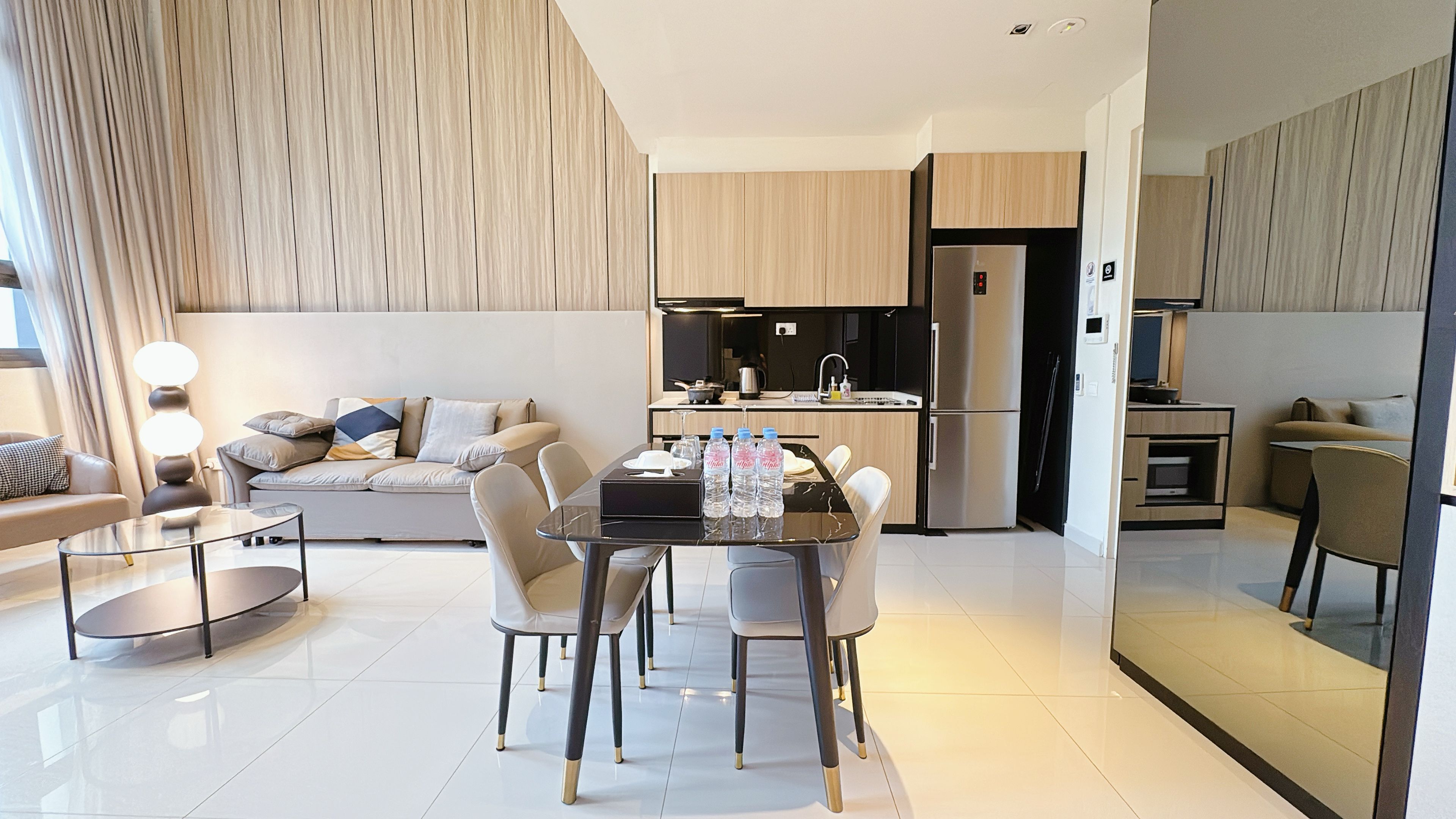 A modern living room with a sofa, a dining table with chairs, and a kitchen area with a refrigerator and stove.