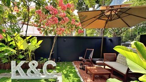 A patio area with a black wall, a wooden bench, a sofa, and a large umbrella.