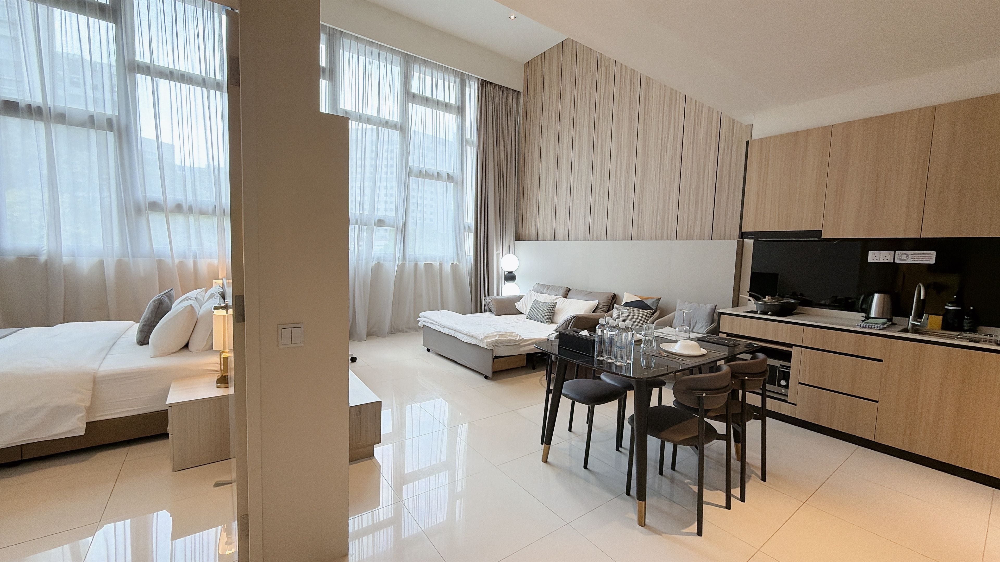 A modern hotel room with a bed, a dining area, and a kitchenette.