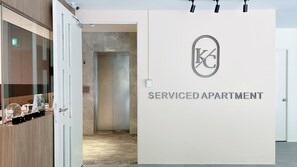A serviced apartment entrance with a sign indicating a fireman access to the 1st floor, a security camera, and a modern design with a tiled floor.