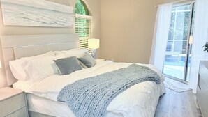 A bedroom with a bed, a nightstand, a window with curtains, and a wall-mounted artwork. - Coastal Paradise Near the Beach - Private Heated Pool - 4BR Marco Island Retreat (Marco Island)