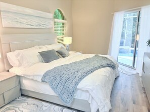 A bedroom with a bed, a nightstand, a window with curtains, and a wall-mounted artwork. - Coastal Paradise Near the Beach - Private Heated Pool - 4BR Marco Island Retreat (Marco Island)