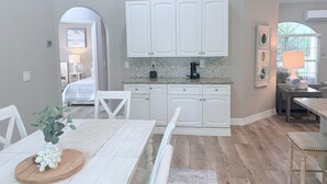 A modern kitchen with white cabinets, a coffee maker, and a dining area with a table and chairs. - Coastal Paradise Near the Beach - Private Heated Pool - 4BR Marco Island Retreat (Marco Island)