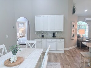 A modern kitchen with white cabinets, a coffee maker, and a dining area with a table and chairs. - Coastal Paradise Near the Beach - Private Heated Pool - 4BR Marco Island Retreat (Marco Island)