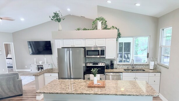 A modern kitchen with a large island, stainless steel appliances, and a dining area with a gray sofa. - Coastal Paradise Near the Beach - Private Heated Pool - 4BR Marco Island Retreat (Marco Island)
