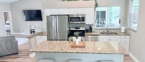 A modern kitchen with a large island, stainless steel appliances, and a dining area with a gray sofa.