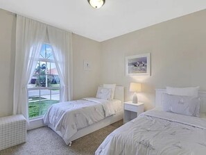 A room with two beds, a window with curtains, a bedside table with a lamp, and a framed picture on the wall. - Coastal Paradise Near the Beach - Private Heated Pool - 4BR Marco Island Retreat (Marco Island)