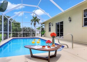 A poolside area with a table set for breakfast, a glass enclosure, and a view of the surrounding landscape. - Coastal Paradise Near the Beach - Private Heated Pool - 4BR Marco Island Retreat (Marco Island)