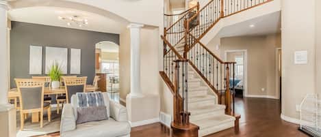 A spacious living area with a staircase, a dining area, and a view into another room.