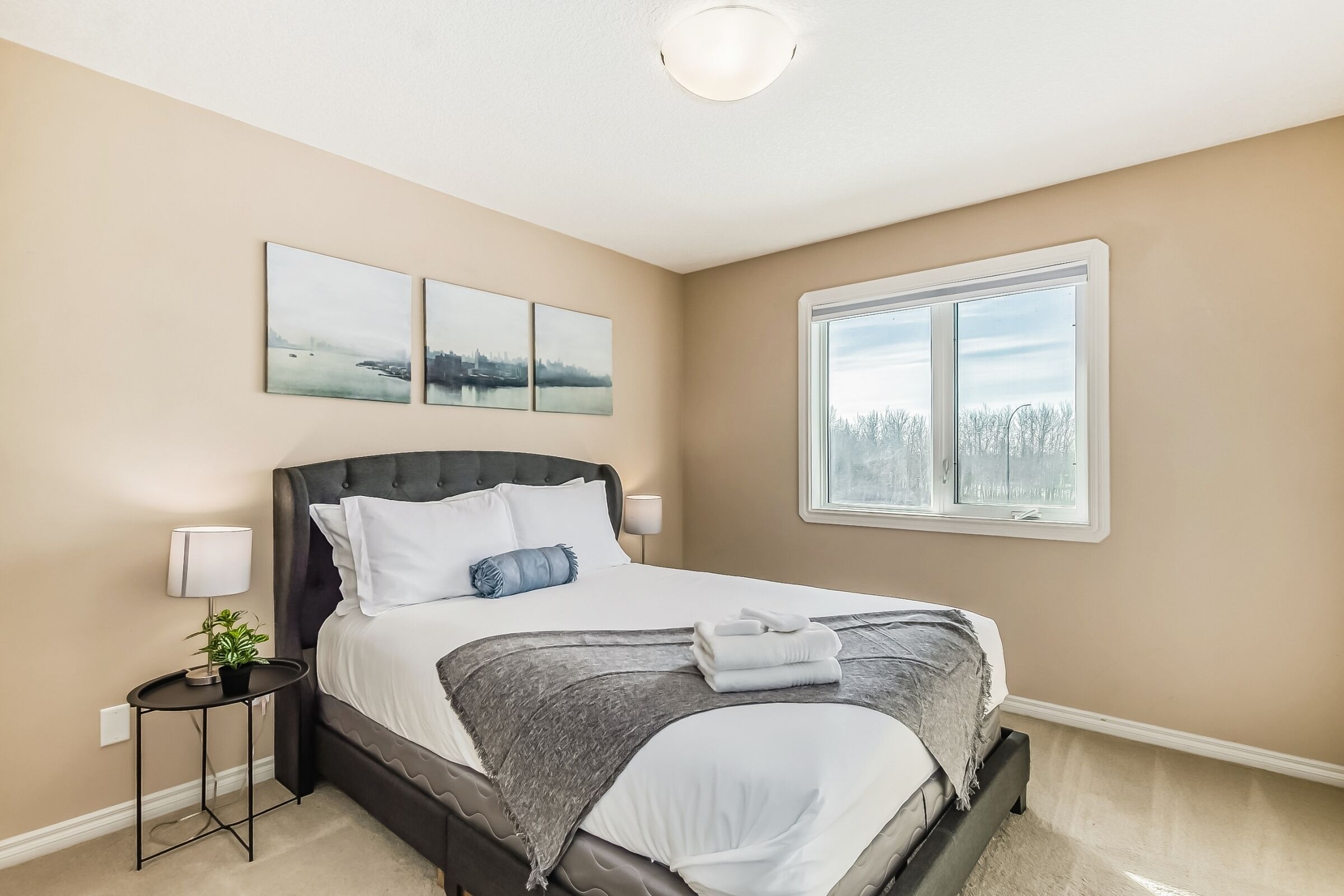 A bedroom with a bed, a nightstand, a lamp, and a window.