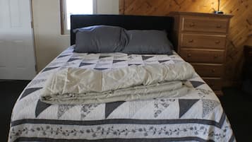 A bed with a quilt, pillows, and a wooden dresser.
