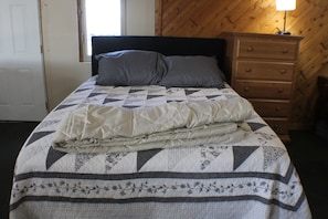 A bed with a quilt, pillows, and a wooden dresser.
