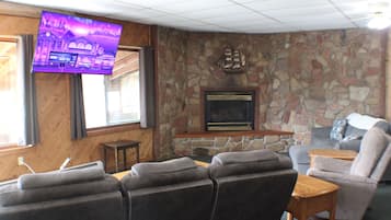 Een woonkamer met een stenen muur, een open haard, een aan de muur bevestigde televisie en een zithoek met een bank en fauteuils.