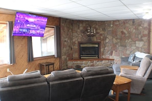 A living room with a stone wall, a fireplace, a television mounted on the wall, and a seating area with a sofa and chairs.
