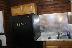 A kitchen with wooden cabinets, a black refrigerator, a granite countertop, and a stainless steel sink.