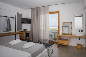 Hotelkamer met een bed, een bureau met spiegel, een klein tafeltje, een stoel, een televisie en een balkon met uitzicht.
