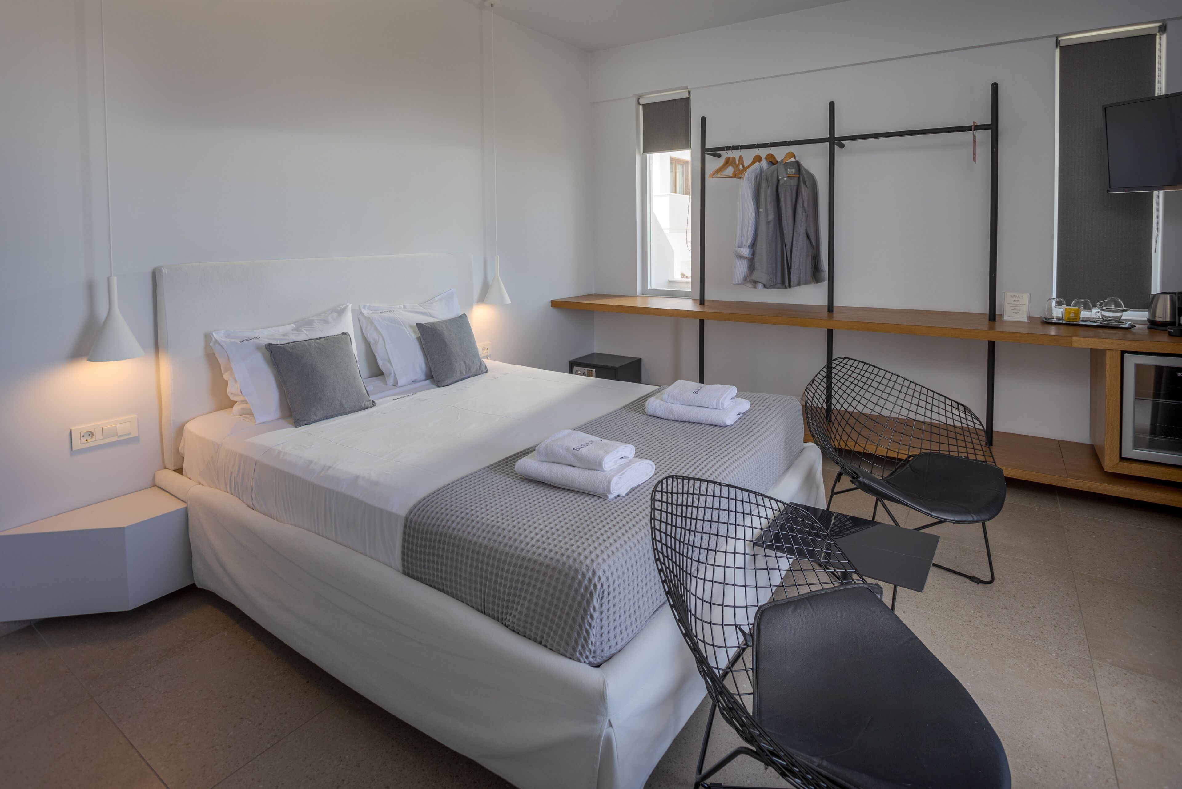 A modern hotel room with a bed, bedside tables, a desk, chairs, and a mirror.