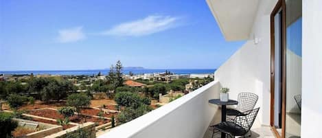 A balcony with a table and chairs, overlooking a coastal landscape with buildings and trees.