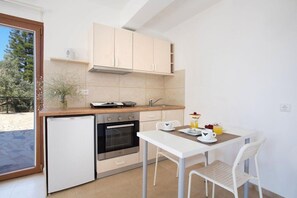 Een kleine keuken met een koelkast, oven en een eettafel met stoelen.