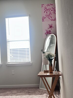Um quarto com janela, espelho, um vaso com flores e um objeto decorativo na parede.