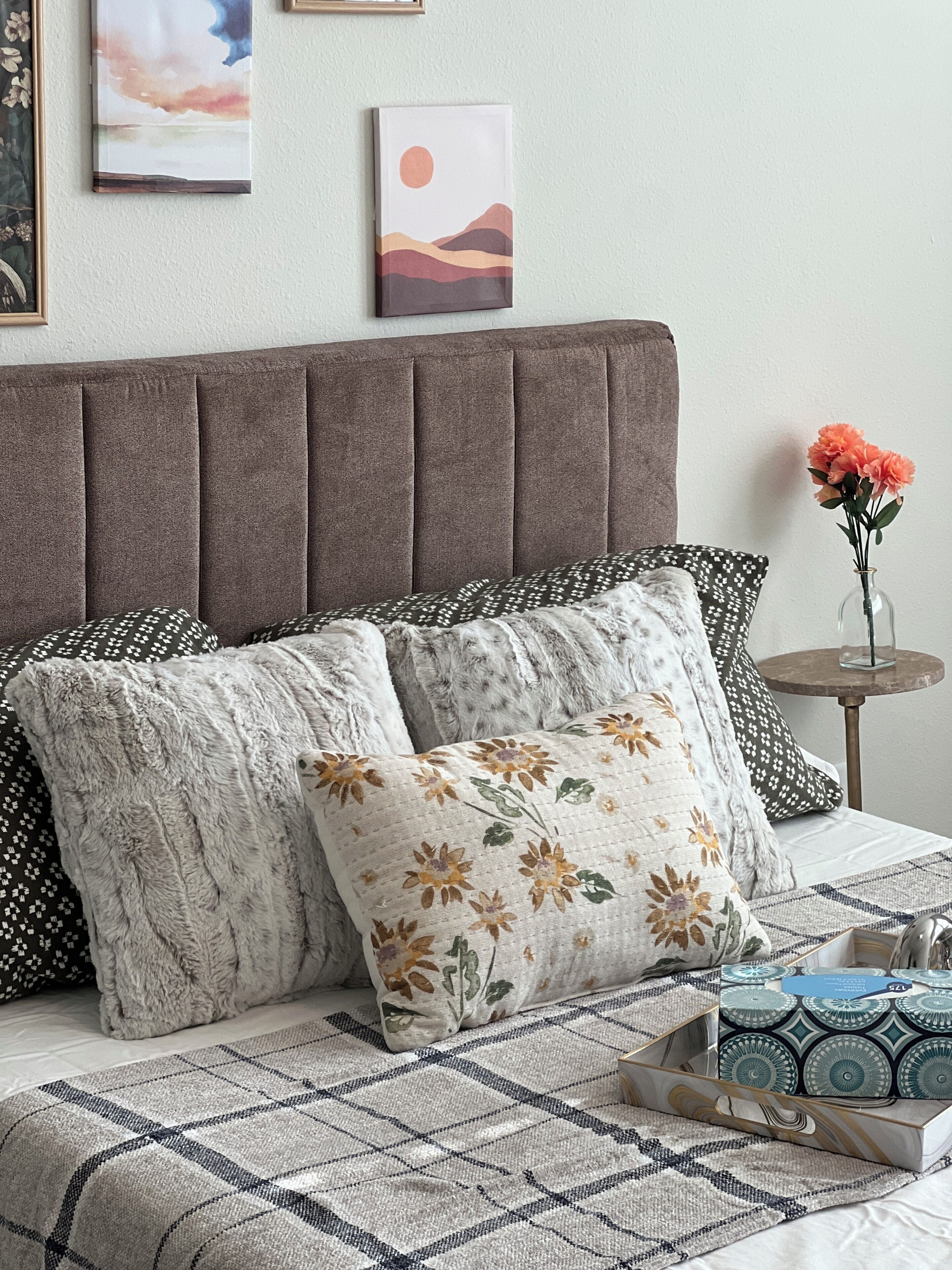 Un lit doté d’une tête de lit rembourrée de couleur grise, de coussins à motifs et d’une couvre-lit à carreaux.
