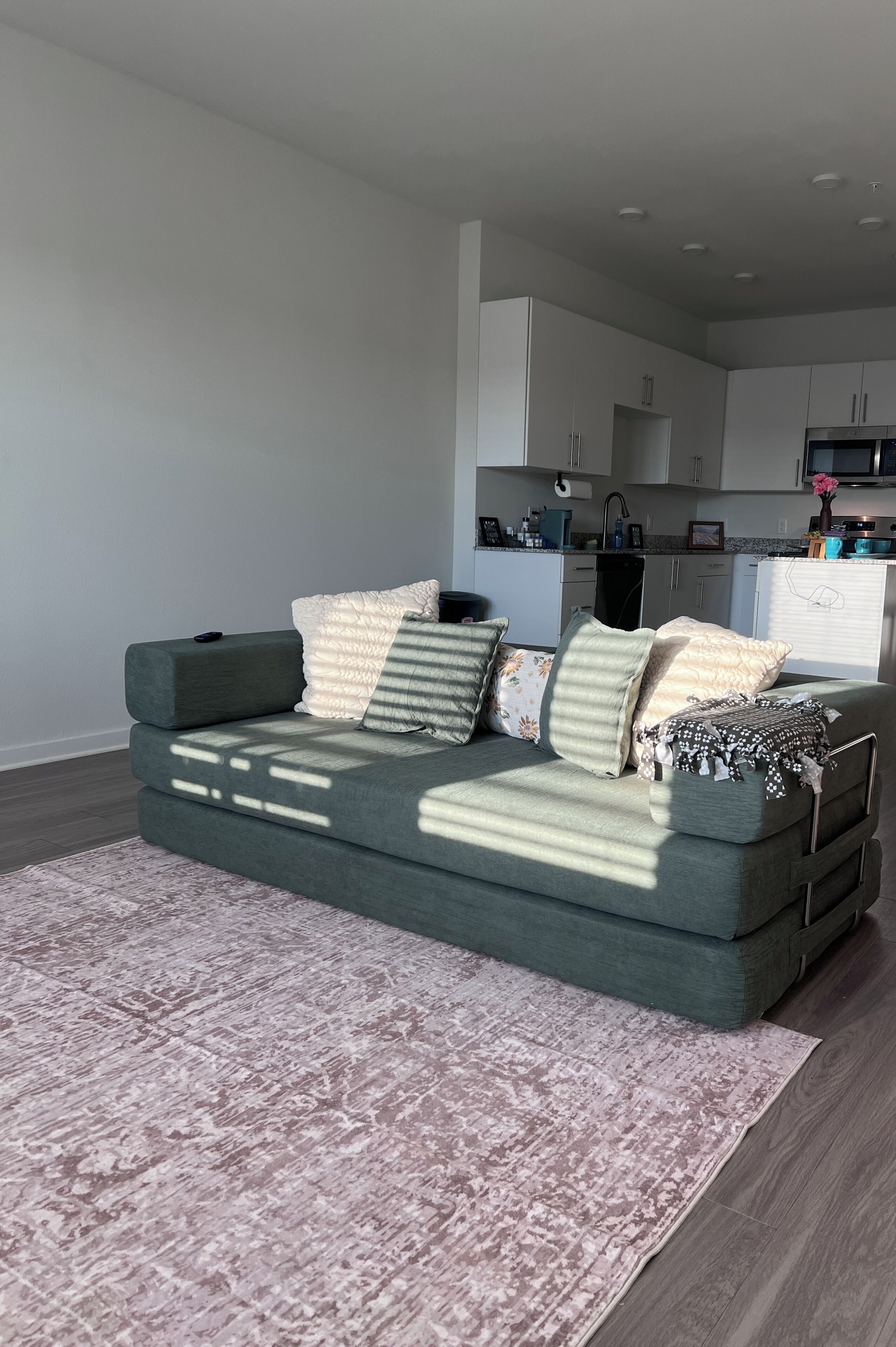 Un salon moderne avec un canapé d’angle, un tapis à motifs et une cuisine en arrière-plan.