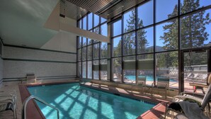 An indoor swimming pool with clear views of the outdoors, surrounded by lounge chairs and a tiled wall.