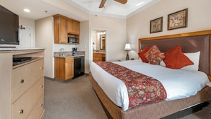 A hotel room with a bed, a ceiling fan, a kitchenette, and a television.