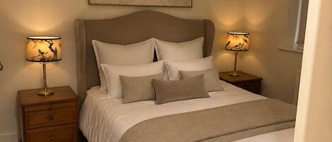 A bedroom with a bed, two bedside tables, a nightstand, a hanging lamp, and a framed picture on the wall.
