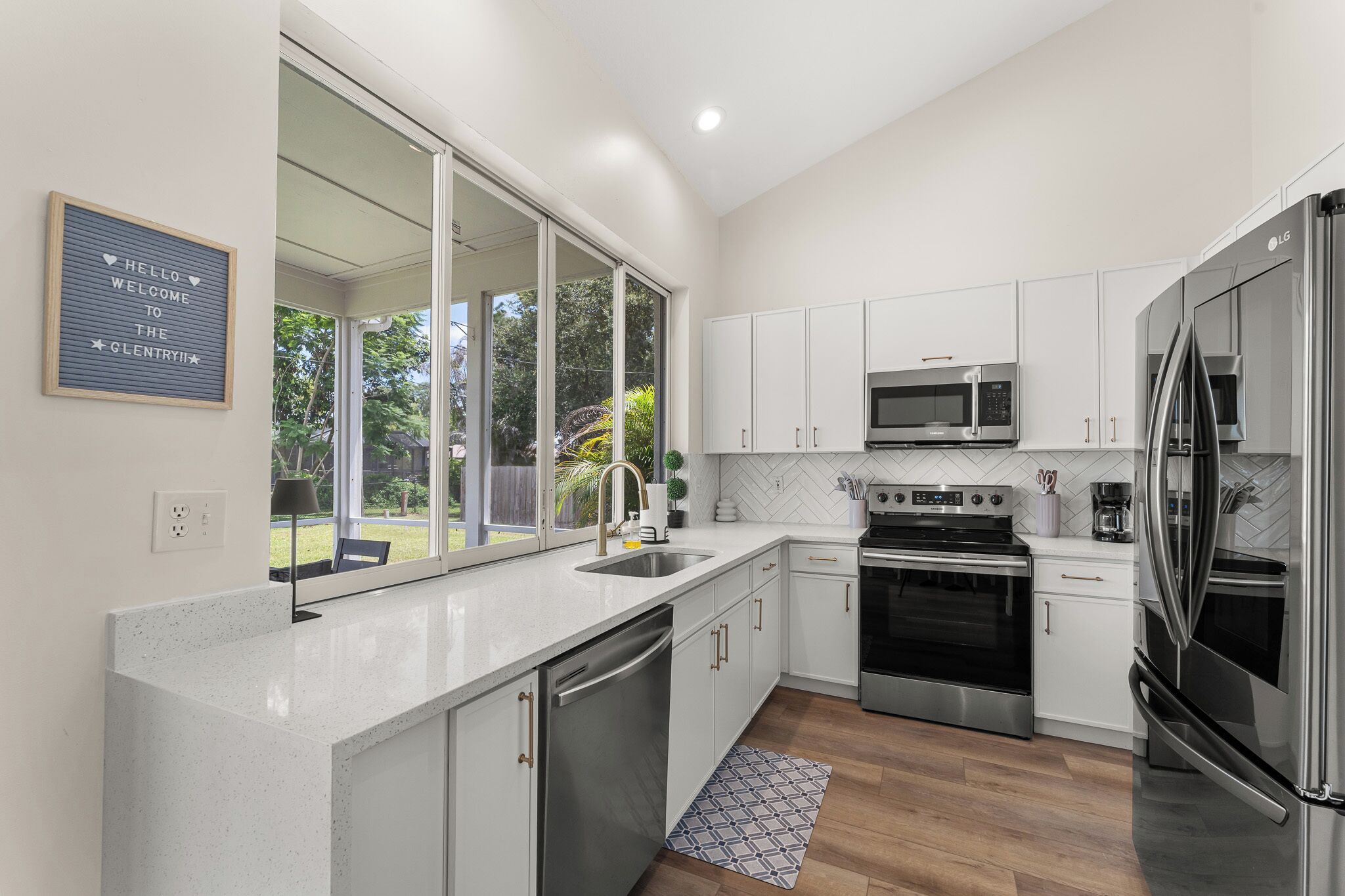A modern kitchen with white cabinets, stainless steel appliances, and a large window.