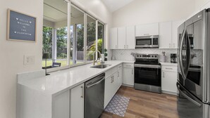 Una cocina moderna con armarios blancos, electrodomésticos de acero inoxidable y un amplio ventanal.