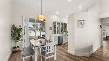 A modern kitchen with white cabinets, a stainless steel refrigerator, and a dining area with a wooden table and chairs.