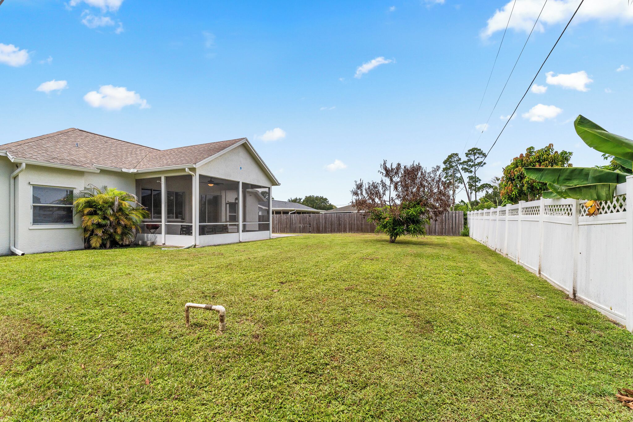 A residential property with a covered patio, a fenced yard, and a house with a sloped roof.