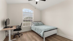 Un dormitorio con escritorio, silla, cama y ventilador de techo.