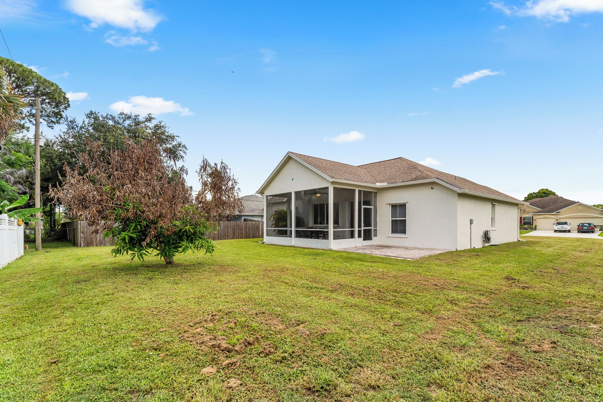 A single-story house with a covered porch, a fenced yard, and a tree.