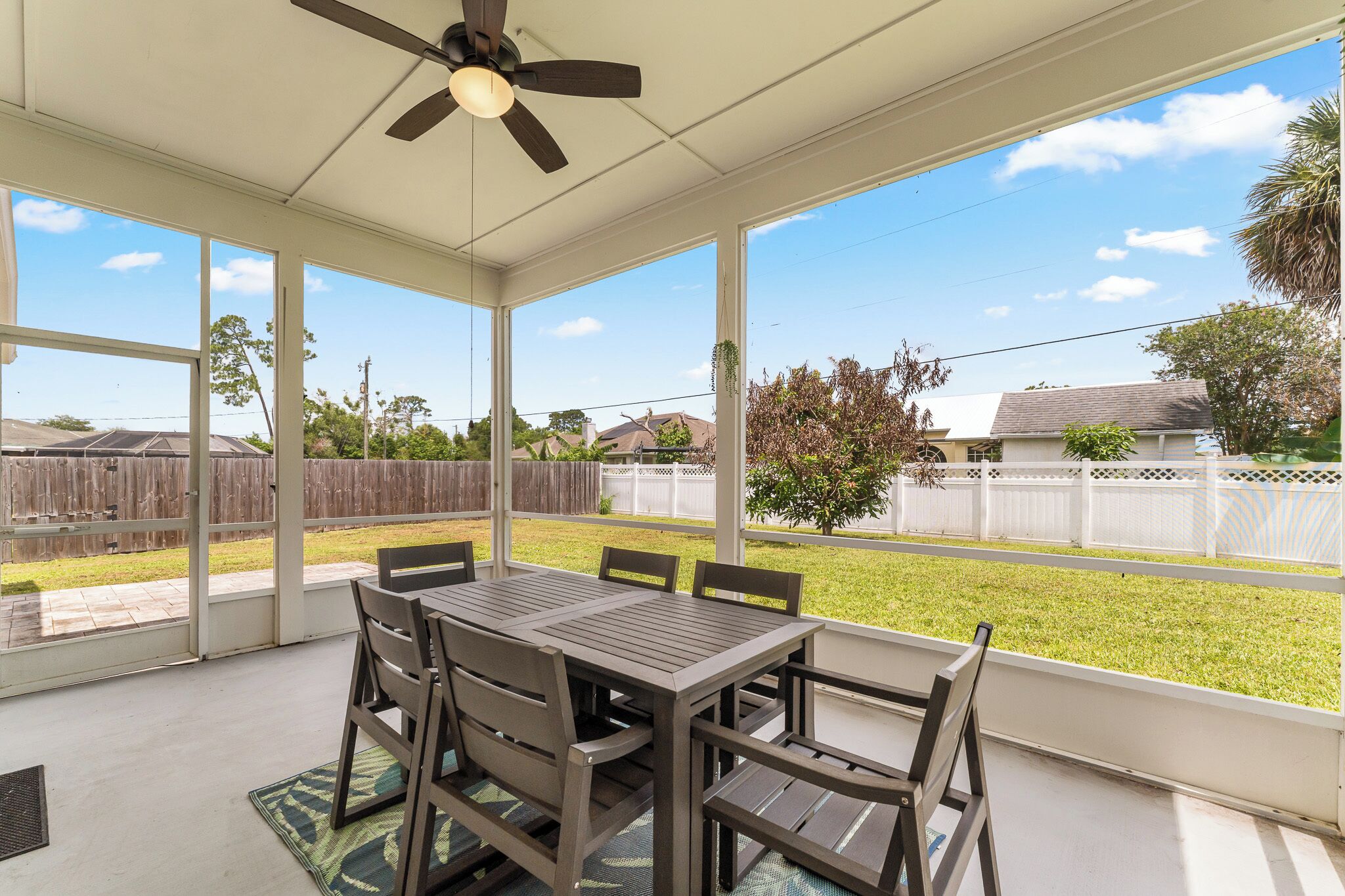 A covered patio with a table and chairs, large windows, and a ceiling fan.