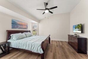 A bedroom with a bed, a ceiling fan, a TV, and a window with blinds.