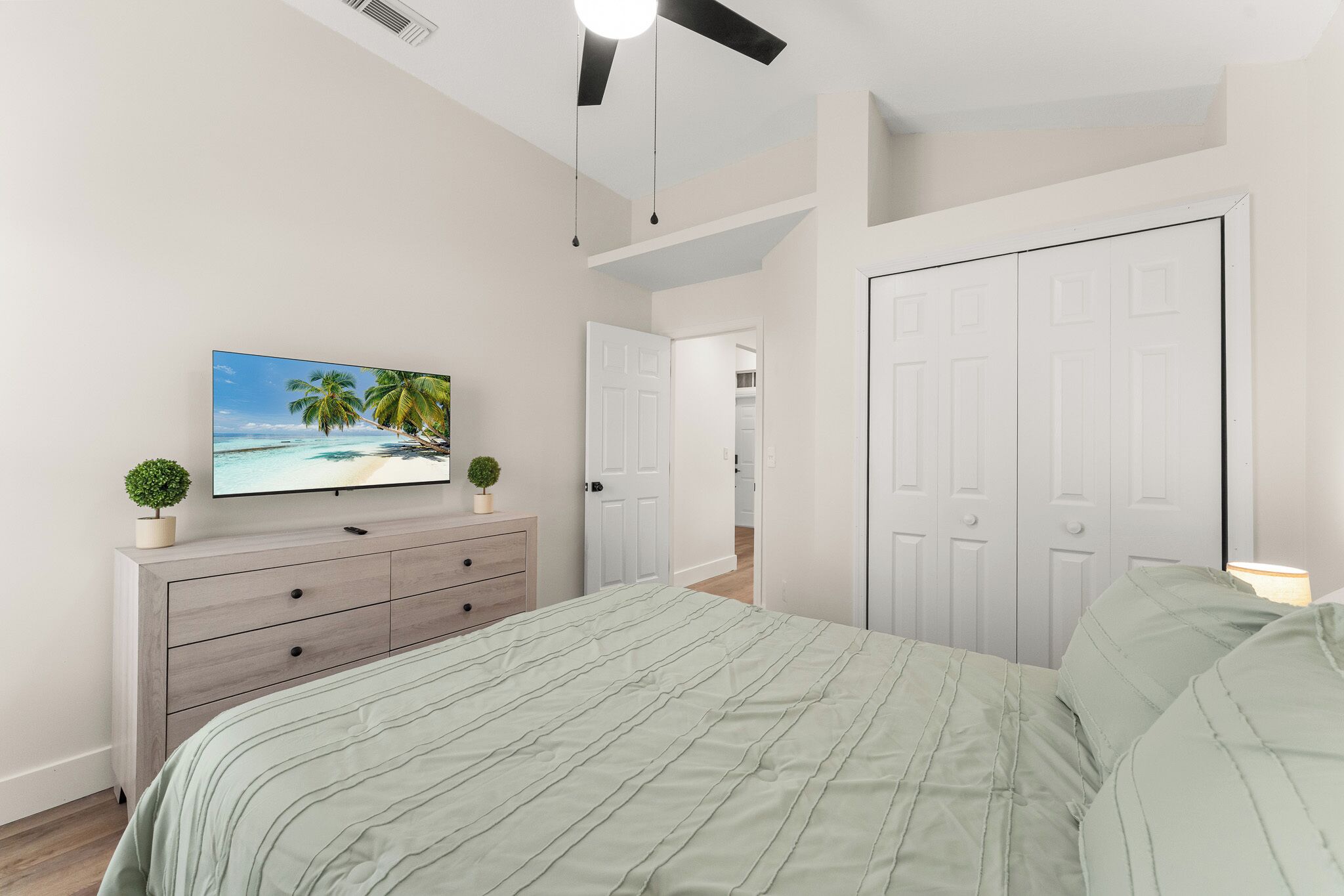 A bedroom with a bed, a dresser, a television, and a door.