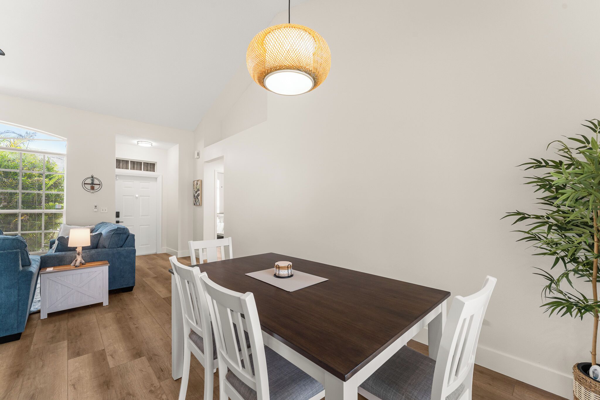 A dining area with a wooden table and white chairs, a hanging light fixture, and a potted plant.